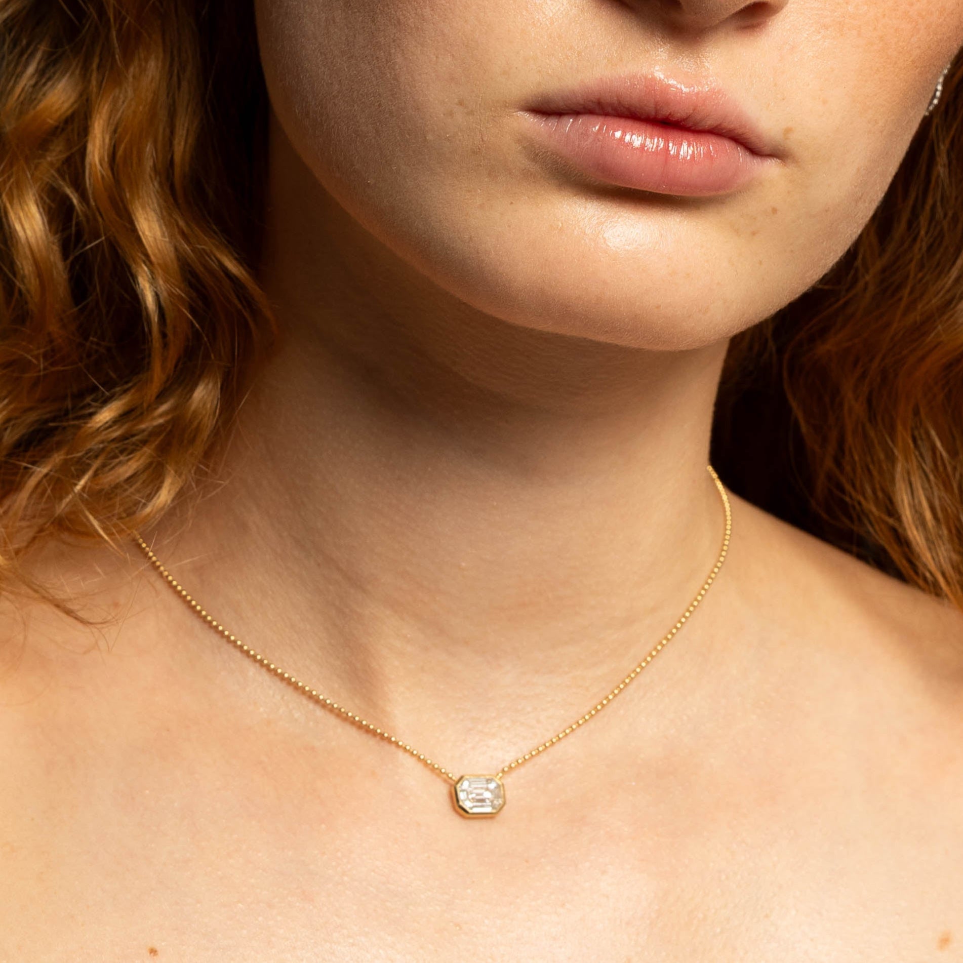 Woman with red hair wearing a gold necklace against a black background